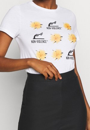 Biała bawełniana koszulka z graficznymi nadrukami żółtych kwiatów oraz czarnym wzorem pistoletu z napisem "NIEPRZEMOC" w powtarzającym się wzorze.