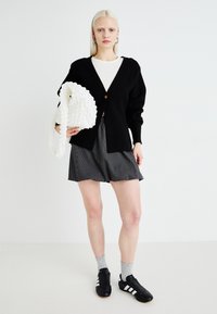 Black cardigan with a single button, white t-shirt, gray striped shorts, gray socks, and black shoes with white stripes. White textured bag.