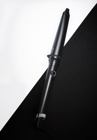 Zwarte krultang met een taps toelopende cilinder en aan-uit knop, diagonaal geplaatst op een zwart-witte gesplitste achtergrond.
