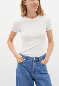 T-shirt bianco a righe con maniche corte abbinato a jeans in denim azzurro chiaro a vita alta con tasche laterali e chiusura con bottoni.
