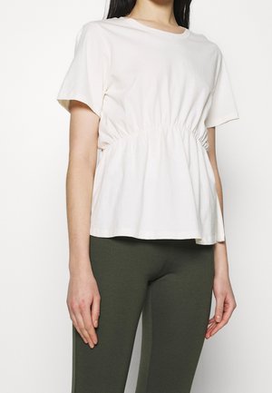 Haut en coton de couleur crème avec manches courtes, taille froncée et coupe décontractée, associé à des leggings vert foncé.