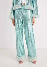 Σετ με δύο κομμάτια κεντημένο με παγιέτες σε τιρκουάζ, περιλαμβάνει ένα κοντό σακάκι με γούνα και παντελόνι με φαρδιά πόδια και ταιριαστά γούνινα μανίκια.