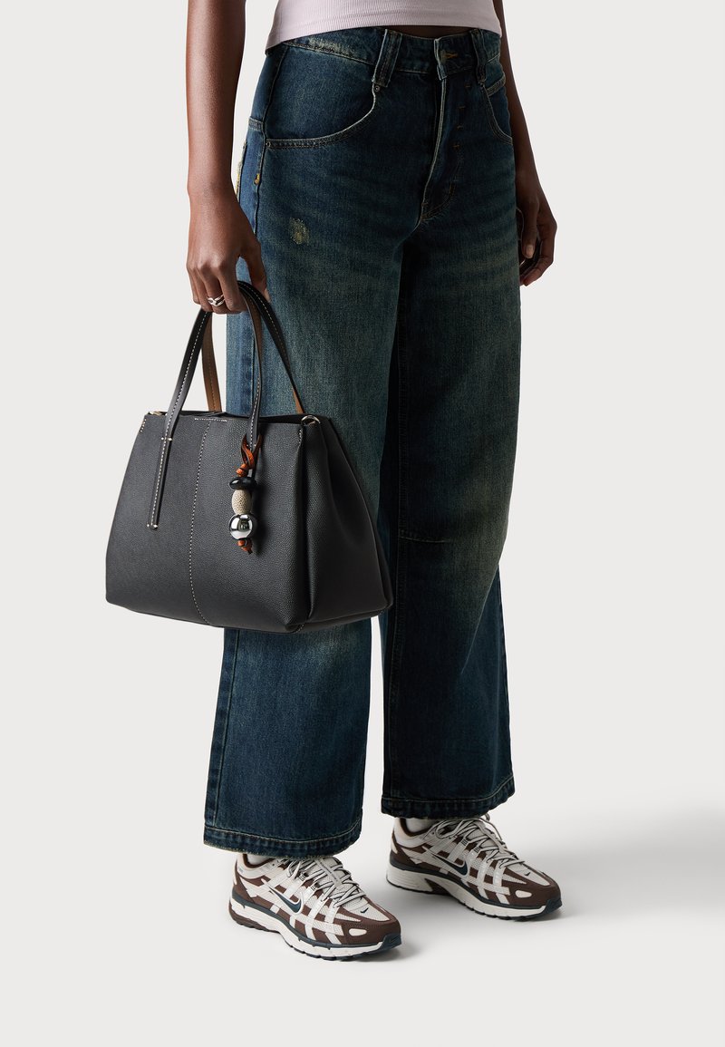 Borsa in pelle nera con forma strutturata, accentuata da un portachiavi decorativo, abbinata a un paio di jeans in denim blu larghi e sneakers con motivo.