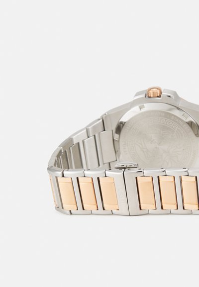 Sidabrinis ir auksinis metalinis laikrodis su nerūdijančio plieno juostele, dekoruota aukso akcentais. Apvalus korpusas su tekstūruota karūna ir graviruotu dugnu.