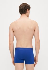 Μπλε βαμβακερά μποξεράκια με εφαρμοστή γραμμή, με αντίθετη μέση που έχει λευκή ρίγα. Οπίσθια όψη της πλάτης και των ώμων του μοντέλου.