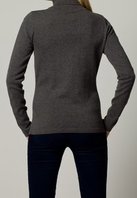 Maglione grigio a collo alto realizzato in un morbido materiale a maglia, con maniche lunghe e colletto a costine, abbinato a jeans scuri attillati.