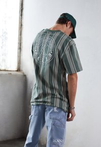 Grönrandig t-shirt med en vit cirkulär logga på baksidan, kombinerad med ljusblå cargobyxor med detaljer och fickor.