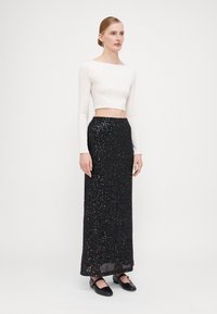 Witte lange mouw cropped top gecombineerd met een zwarte pailletten maxi rok. De rok heeft een gestructureerd oppervlak en een rechte silhoët.