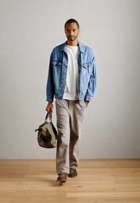 Chaqueta de denim sobre una camisa blanca, pantalones beige. Llevando un bolso verde. Suelo de madera y fondo neutro. Atuendo casual, corte relajado.