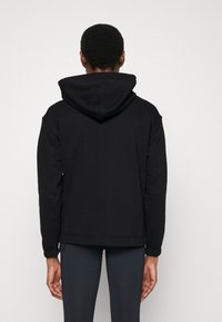 Felpa con cappuccio nera, dal taglio comodo, con una texture liscia e polsini a coste. Dalla vista posteriore non sono visibili loghi o motivi.