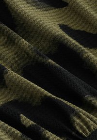 Tissu texturé arborant un motif camouflage vert et noir, avec un tissage en style nid d'abeille et une finition douce et mate.