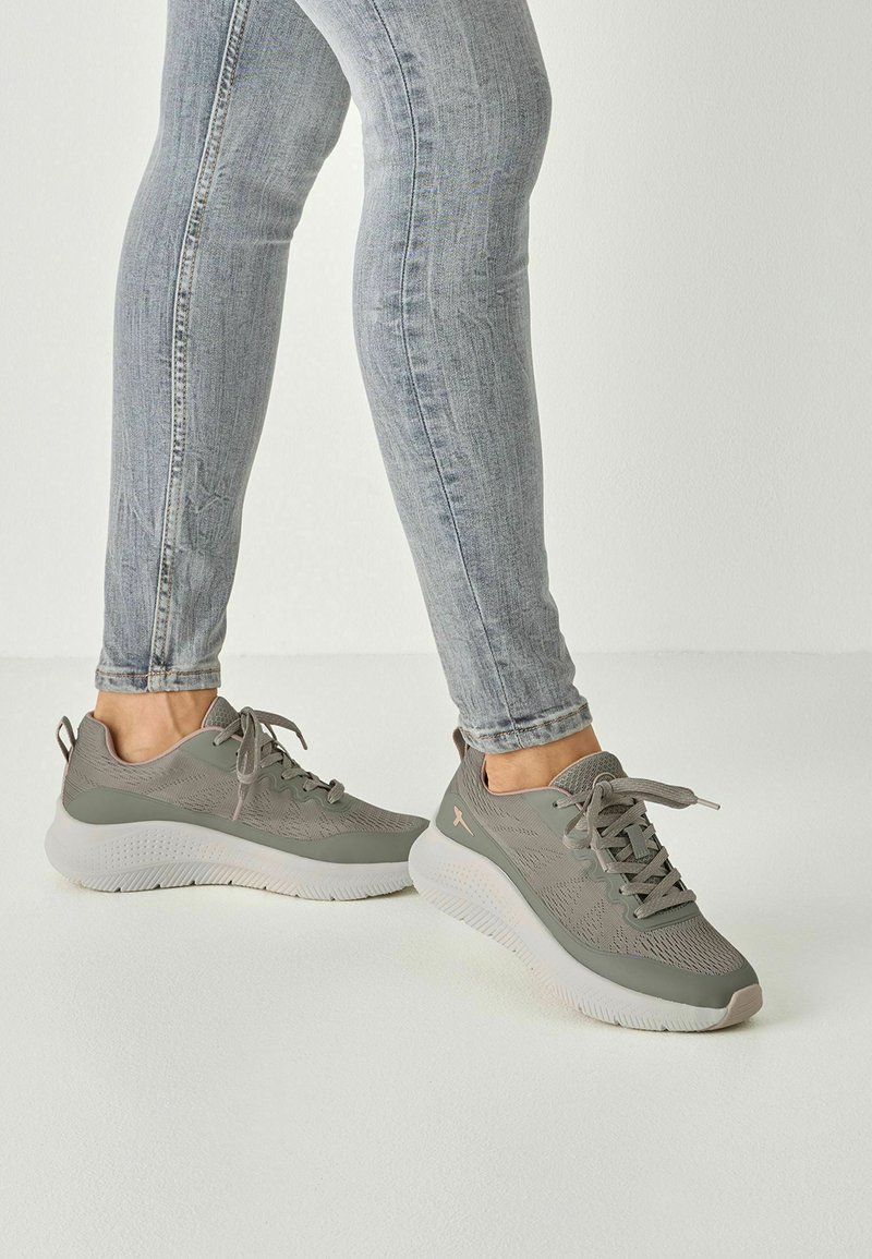 Jasnoszare sportowe trampki z teksturowaną siateczkową cholewką, białą amortyzowaną podeszwą i subtelnym różowym akcentem na pięcie, w sznurowanym stylu.