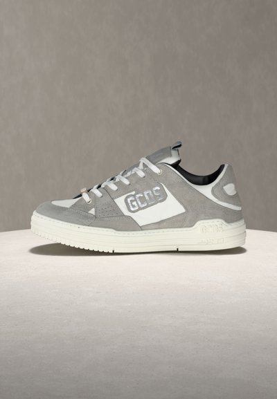 Αθλητικό παπούτσι χαμηλού πάτου σε γκρι και λευκό σουέτ και δέρμα με λευκά κορδόνια και λογότυπο "GCDS" στο πλάι και στη σόλα, εκτεθειμένο σε στρογγυλή επιφάνεια.