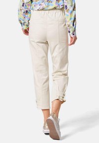 Hellbeige, cropped Hosen mit glatter Textur und aufgerolltem Saum. Kombiniert mit goldenen Sneakers, die ein lässiges Design zeigen.