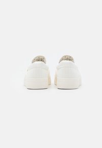Baskets en toile blanches avec une semelle en caoutchouc beige, dotées d'un col rembourré et d'un design minimaliste, vues de l'arrière.