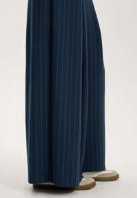 Mornarsko široke hlače narejene iz gladkega materiala z diskretnimi belimi črtami. Imajo sproščen kroj in mehak pas.