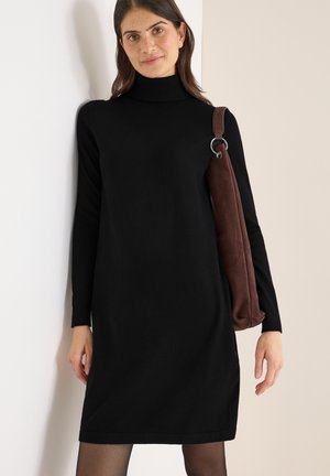 Schwarzes Rollkragenkleid aus einem weichen Strickstoff, kombiniert mit einer braunen Wildleder-Schultertasche mit silbernem Ringbeschlag.