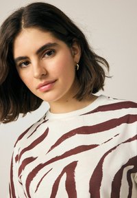 Weißes T-Shirt mit kräftigen, kastanienbraunen Zebra-Streifen, featuring einem Rundhalsausschnitt und weichem, strukturiertem Baumwollstoff. Minimalistisches Design.