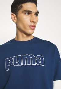 Navy blue sweatshirt featuring a large white embroidered "puma" logo, round neckline, short sleeves, and a soft texture.