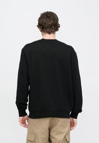 Felpa nera con collo rotondo, spalle scese e polsini e orlo a coste. Tessuto strutturato, design minimalista, senza marchi visibili.