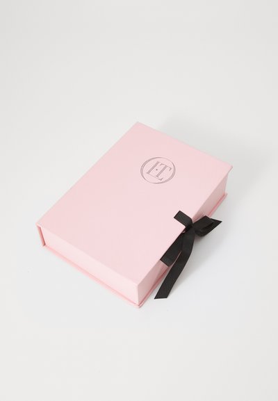 Boîte cadeau rectangulaire rose avec un système de fermeture en ruban noir, présentant un logo circulaire en relief sur le devant. Texture lisse et design robuste.