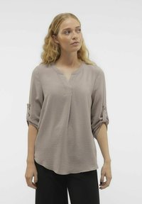 Blusa di un tenue taupe con scollo a V, maniche tre quarti con risvolti e un tessuto testurizzato. Vestibilità ampia con orlo curvato.