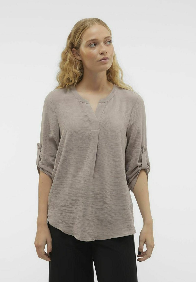 Blusa di un tenue taupe con scollo a V, maniche tre quarti con risvolti e un tessuto testurizzato. Vestibilità ampia con orlo curvato.