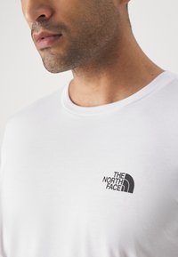 White cotton t-shirt featuring a black logo printed on the left chest. Round neck design with a smooth texture and short sleeves.