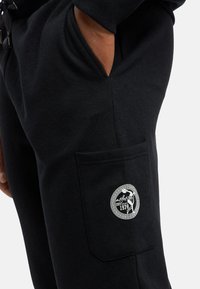 Sorte sweatpants med en sidelomme, der har et rundt hvidt logo-patch. Blødt materiale og en afslappet pasform med elastisk talje.