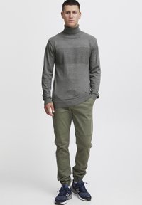 Grey turtleneck sweater with a textured middle stripe, paired with olive pants featuring knee patches and navy sneakers. Minimalistic design.