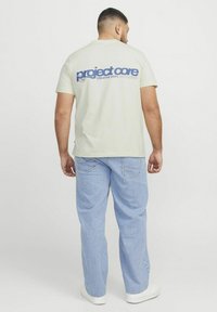 Helebeige puuvillane T-särk, mille seljal on sinine "project core" logo, sobib kergete siniste teksade ja valgete tossudega.