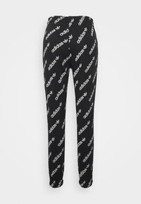 Černé tepláky s opakujícím se bílým vzorem loga Adidas, elastickým pasem a zúženými nohavicemi s manžetami na kotnících.