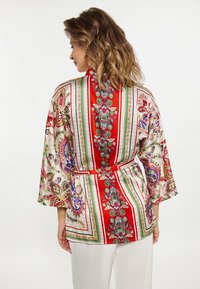 Punane ja mustriga kimono-stiilis jakk, millel on lille- ja paisleedesainid, vöökoht ja kolmeveerandi varrukad. Tekstureeritud kanga viimistlus.