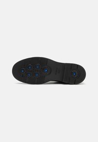 Semelle de chaussure noire avec sept aérateurs d'air circulaires bleus et des grips texturés, marquée "GEOX" et "Brevet italien."