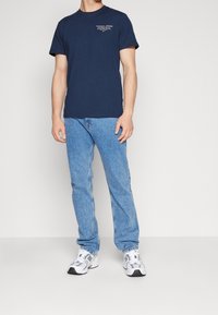 Mörkblå bomullströja med korta ärmar och rund halsringning, i kombination med ljusblå jeans och vita och grå sportskor.