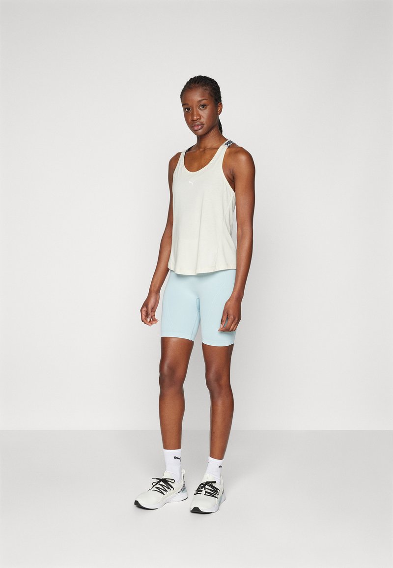Top in cotone grigio chiaro con un design fluido, abbinato a pantaloni corti aderenti azzurri. Gli accessori includono calze bianche e scarpe sportive nere.