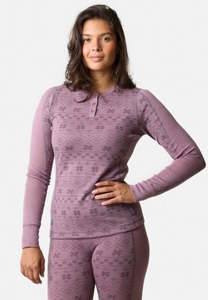 Langærmet top i lyse lilla stof med et mønstret design. Har en henley-udskæring med tre knapper og kontraststing detaljer.