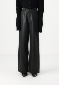 Black leather wide-leg trousers with a high waist, featuring front pockets and a smooth texture, paired with black heeled shoes.