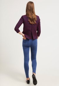 Maroon patterned jacket with three-quarter sleeves, back vent detail, paired with fitted blue denim jeans and black shoes.