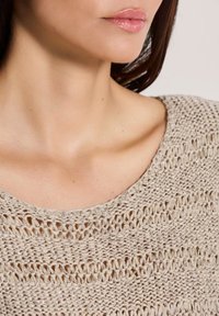 Beige gebreide trui met een losse, open weefpatroon. Heeft een brede, ronde halslijn. Zachte textuur met een subtiele glans van metalen draden.