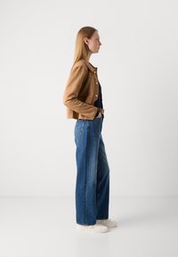 Brun kunstlærjakke med cropped design, sammen med høyt liv og vide blå jeans samt hvite joggesko.