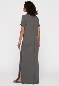 Robe grise, longueur genou, avec des manches retroussées, une coupe droite, fente sur le côté et détail de couture visible le long du dos. Fabriquée en tissu de coton doux.