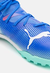 Botas de fútbol azules con una parte superior texturizada, diseño degradado y un destacado logo blanco de Puma. Los cordones son azules y la suela es verde claro.