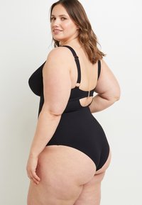 Maillot de bain une pièce noir avec de larges bretelles, tissu texturé et un détail découpé au dos. Présente un design classique adapté à différentes tailles.