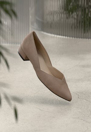 Chaussures en suède beige à talon bas avec un bout pointu et un design en découpes en V. Texture lisse et accent de talon noir contrastant.