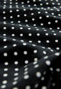 Țesătură neagră cu o textură moale, având buline albe dispuse uniform. Modelul este clasic și contrastează cu fundalul întunecat.