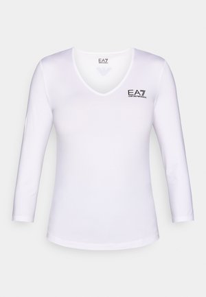 Bela majica z dolgimi rokavi in izrezom v obliki črke V. Na levi strani se nahaja črn logotip EA7. Gladek, lahek material s prilegajočo se obliko.