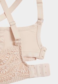 Reggiseno beige chiaro con dettagli in pizzo, spalline regolabili e chiusura a gancetto. Caratterizzato da un tessuto morbido e una texture liscia sui lati.
