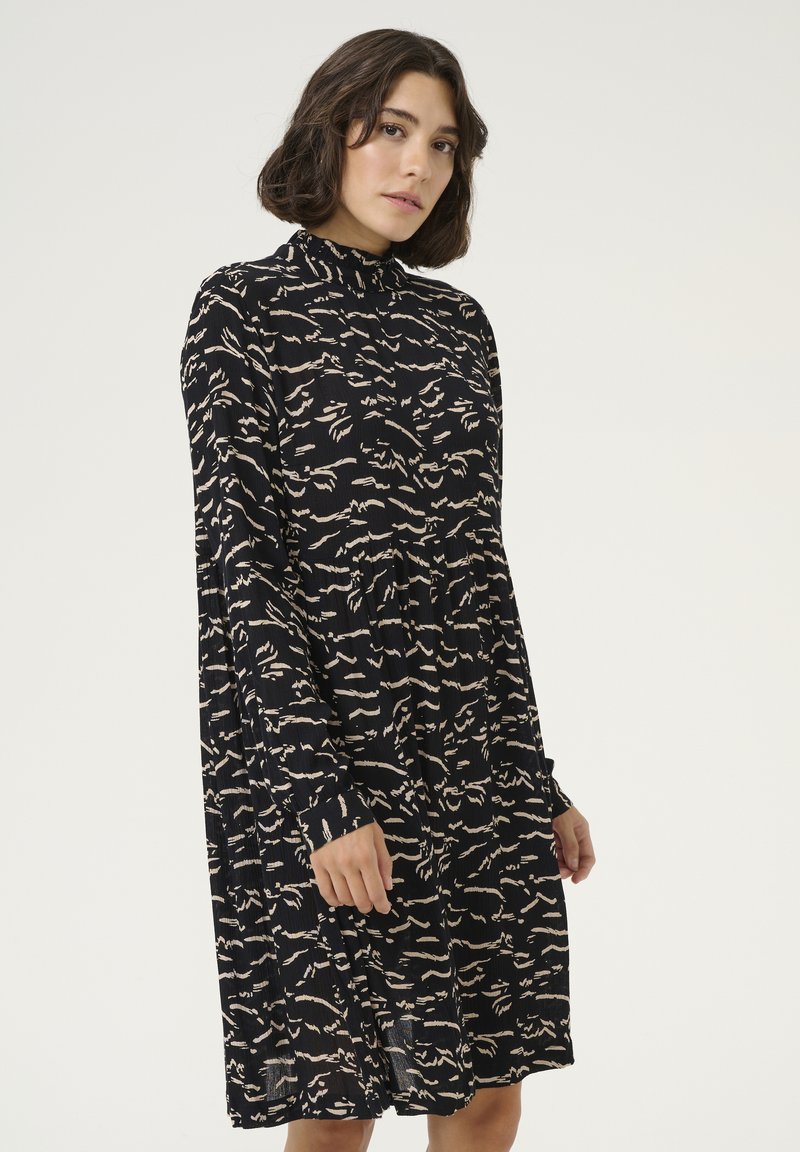 Robe noire avec un col montant, présentant un design plissé et un motif abstrait beige. Manches longues et coupe décontractée. Fabriquée en tissu léger.