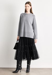 Γκρι πλεκτό πουλόβερ, μαύρη φούστα από τουλ με διακοσμητικά μαργαριτάρια, μαύρα μποτάκια αστραγάλου και μικρή μαύρη τσάντα χειρός. Ομαλή υφή, πολυεπίπεδη εμφάνιση.